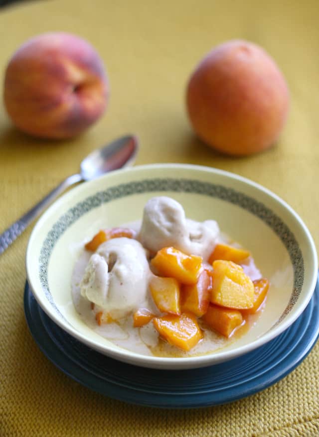 cooked peaches with ice cream in a yellow bowl on a blue plate