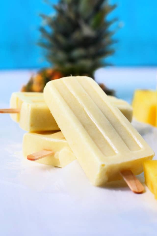 dairy free pina colada popsicles on a white surface with a blue background