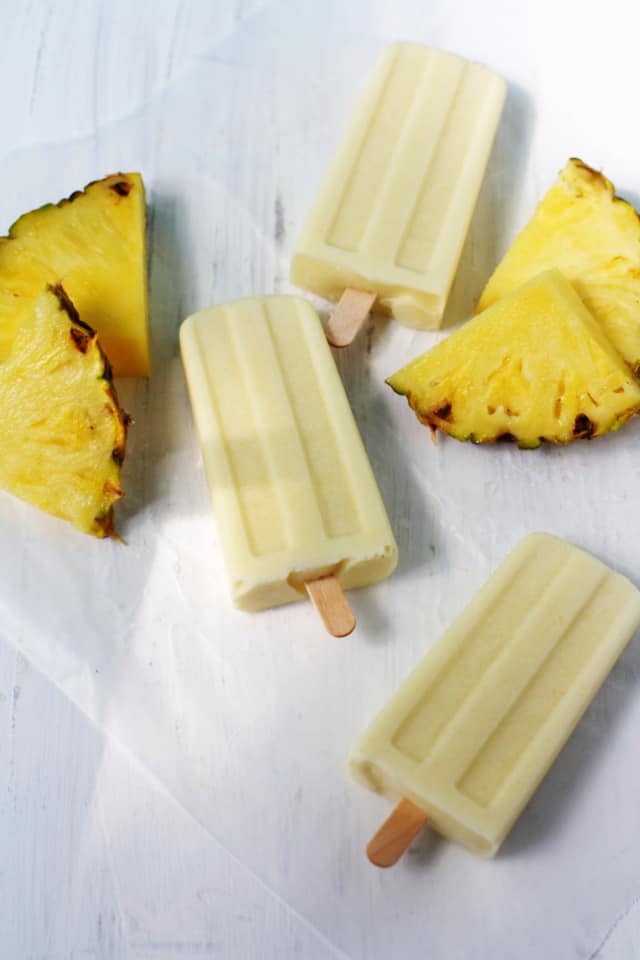 pina colada popsicles on a white background with pineapple slices