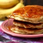 fluffy vegan banana pancakes with maple syrup on a pink plate