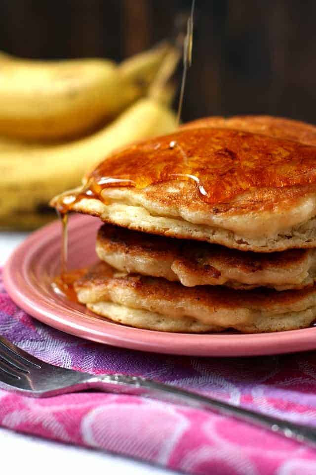 fluffy vegan banana pancakes with maple syrup on a pink plate