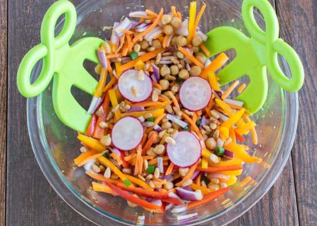 chickpea salad in a glass bowl with green tongs