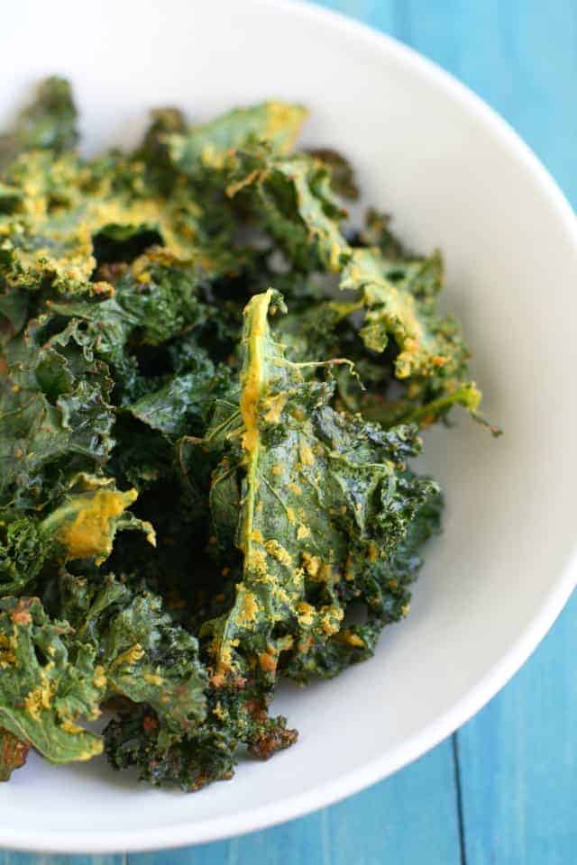 baked kale chips in a white bowl on a blue table