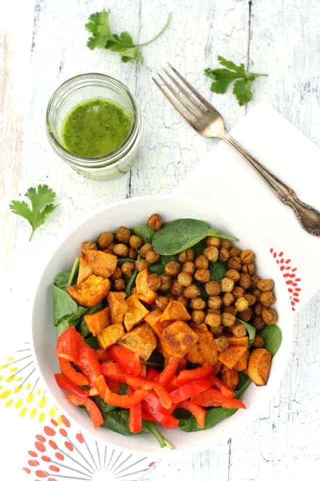 spinach salad topped with roasted sweet potatoes, bell peppers, and chickpeas