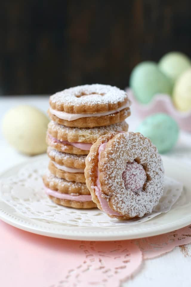 gluten free sugar cookie sandwiches stacked on a white plate with a doily