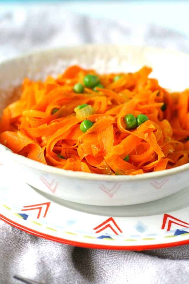carrot noodles with peas and garlic in a white bowl