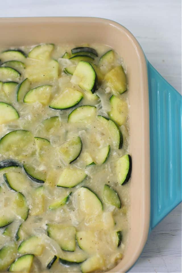 sliced zucchini and onions in a blue casserole dish