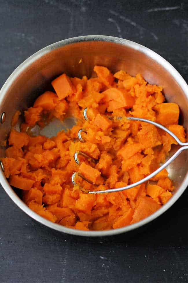 sweet potatoes in a pan with a potato masher