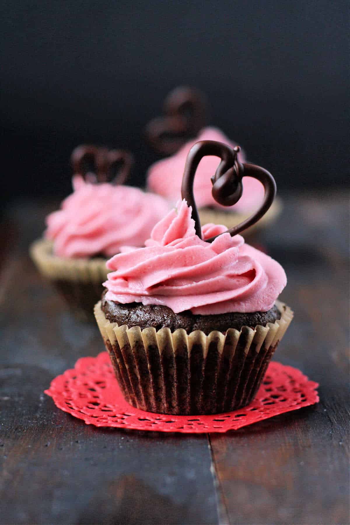 chocolate valentine cupcakes with pink frosting on a red doily
