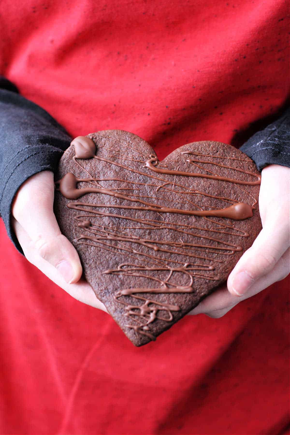large heart shaped chocolate sugar cookie being held in a person's hands