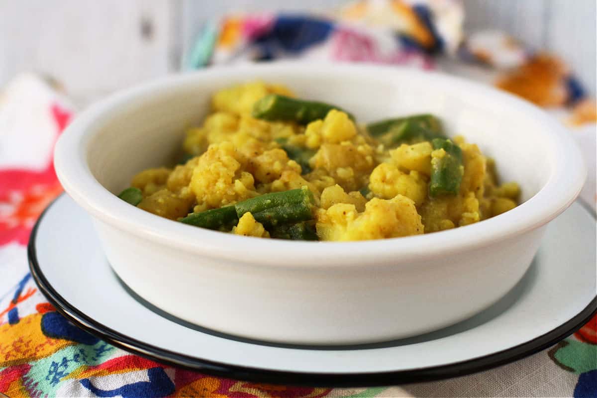 cauliflower potato curry with green beans in a white bowl on a floral napkin