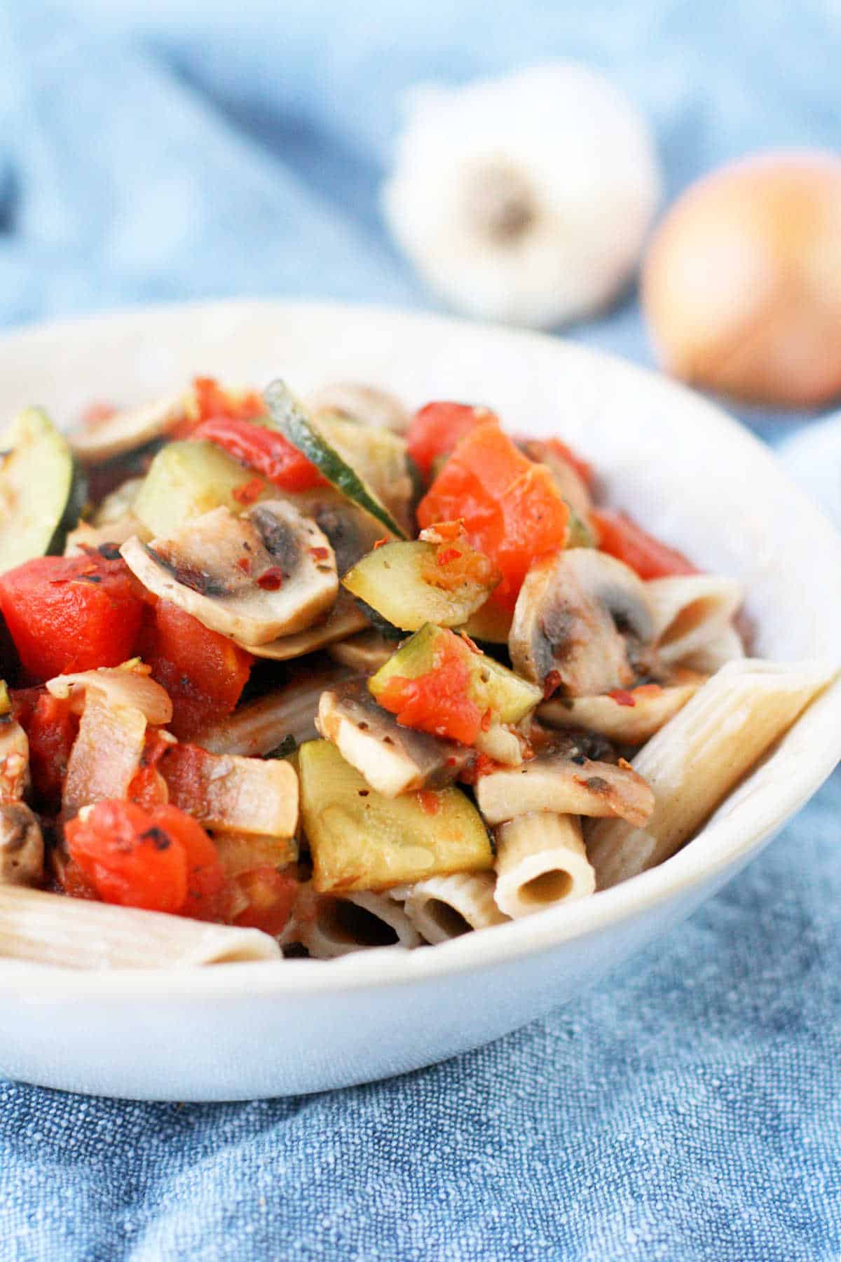 pasta with tomatoes zucchini and mushrooms in a white bowl