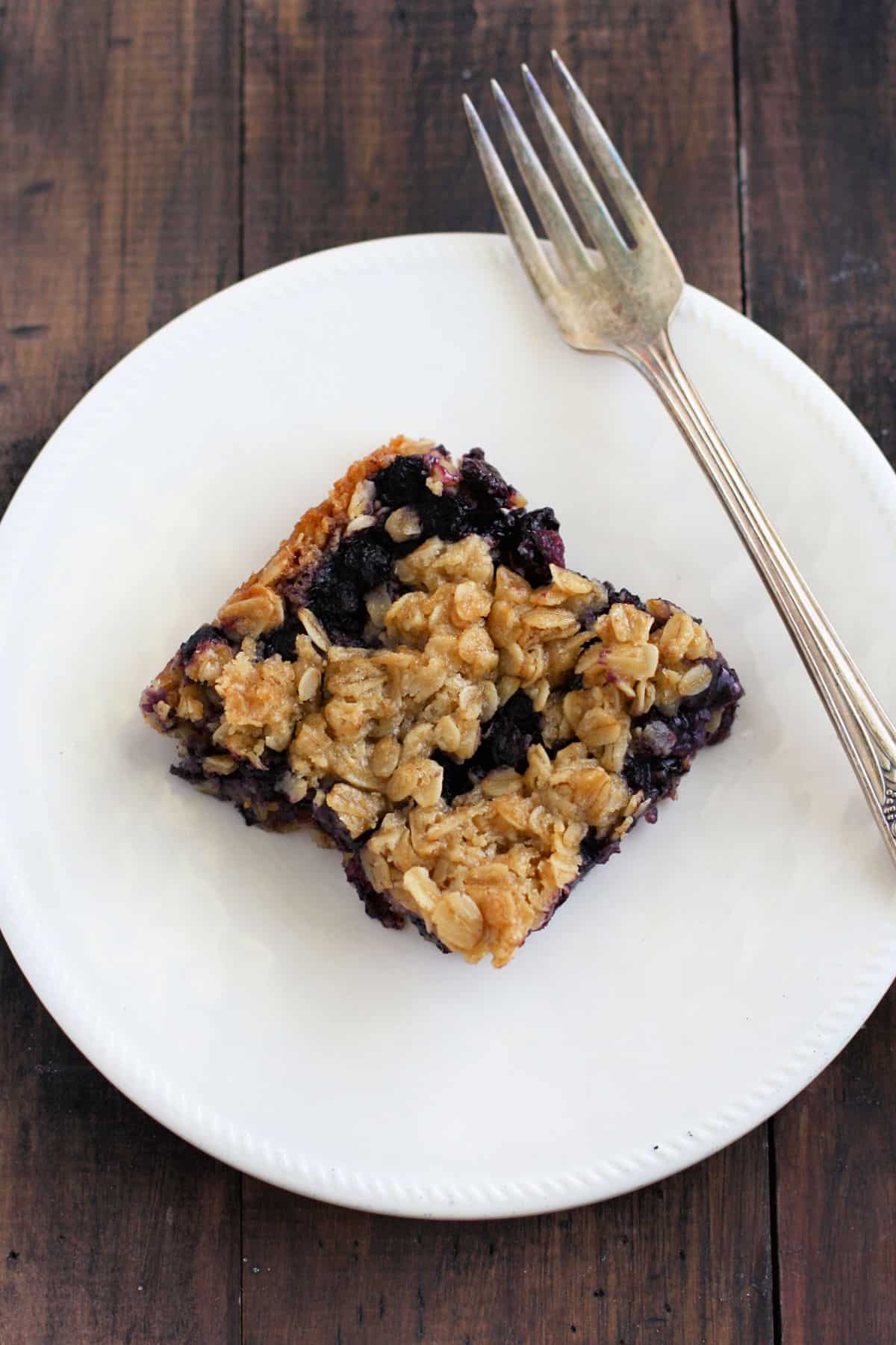 blueberry oat crumb bar on a white plate with a fork