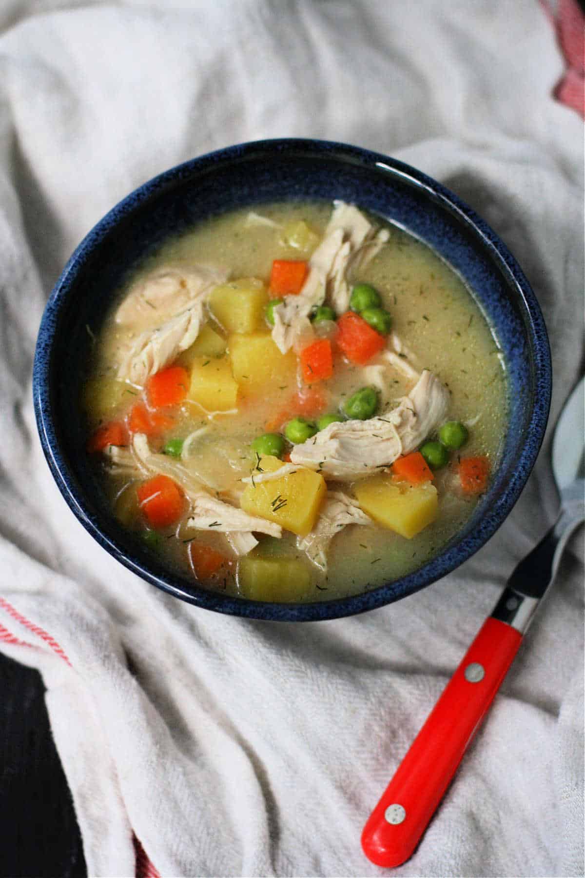 easy chicken pot pie soup with vegetables in a blue bowl with a red spoon