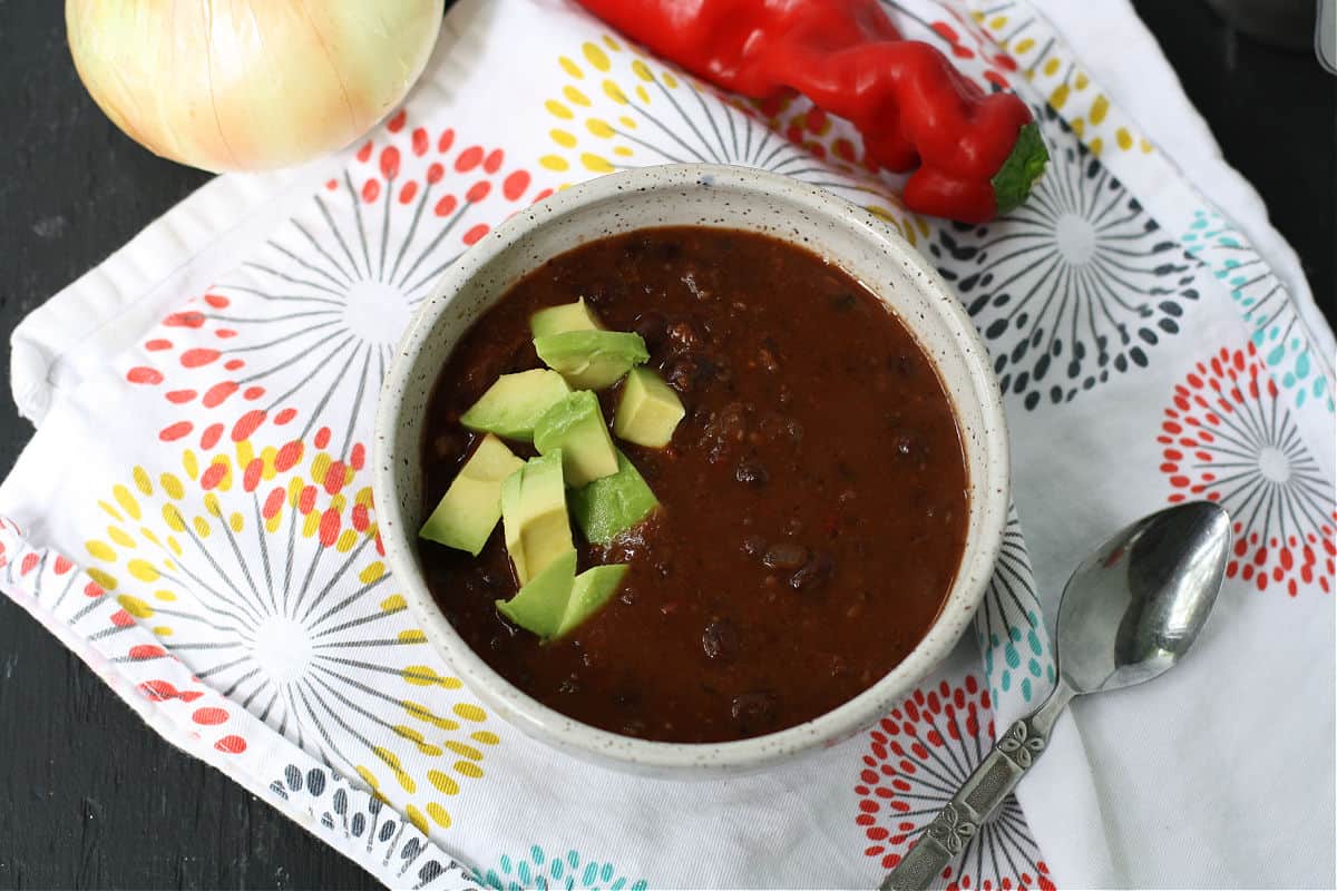 vegan black bean soup in a white bowl topped with avocado