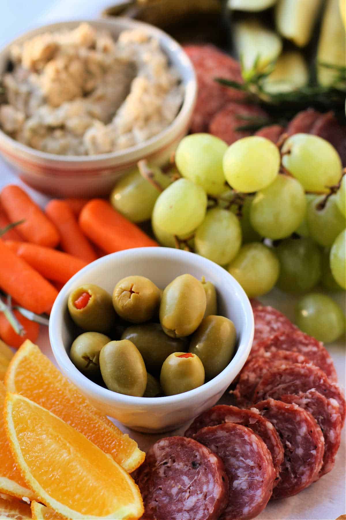 olives salami fruit and bean dip on a wooden board