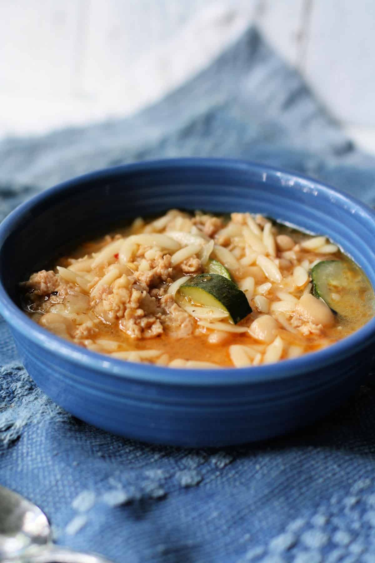 sausage orzo zucchini soup in a blue ceramic bowl